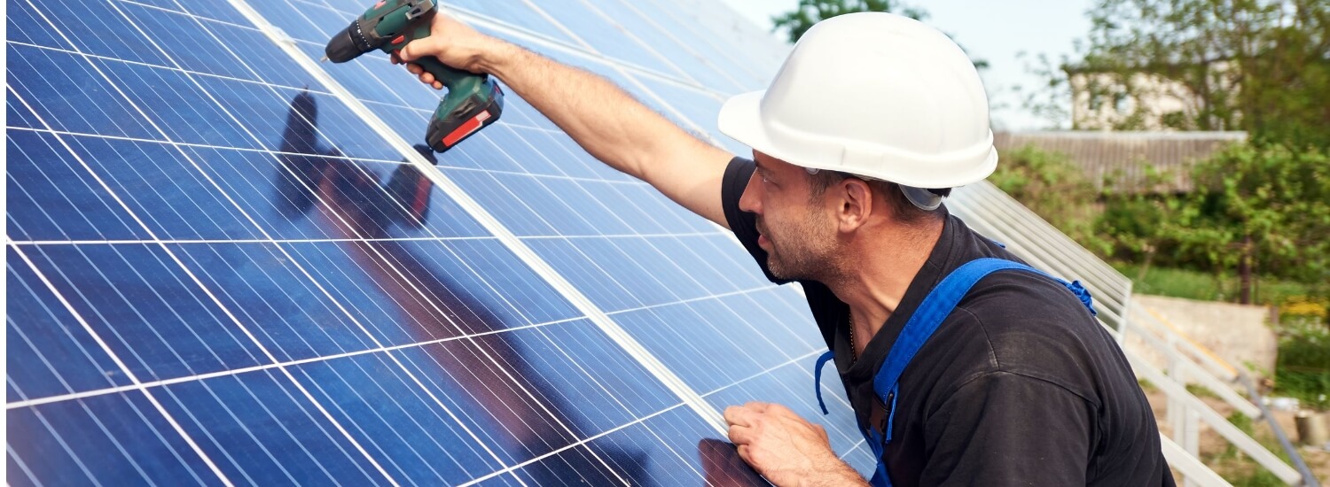 Solar panel technician with drill installing solar panels on roof